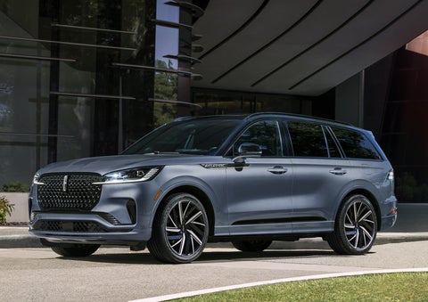 A gray 2025 Lincoln Aviator® SUV is parked outside a modern building showcasing the driver’s side of the vehicle. | Steet-Ponte Lincoln in Yorkville NY