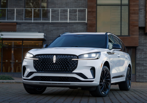 A white 2025 Lincoln Aviator® SUV is shown parked outside a modern building with gray brick and wood accents. | Steet-Ponte Lincoln in Yorkville NY