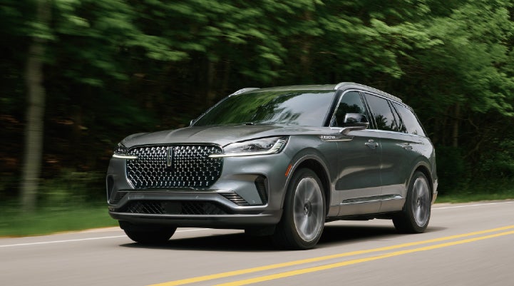 A 2027 Lincoln Aviator® SUV is being driven down a road lined with trees. | Steet-Ponte Lincoln in Yorkville NY