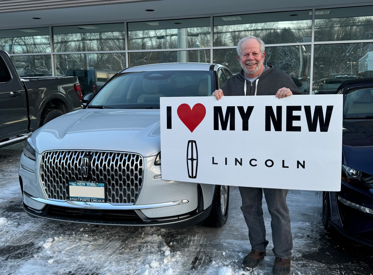 A man in front of a vehicle holding an I love Steet-Ponte Lincoln Lincoln sign