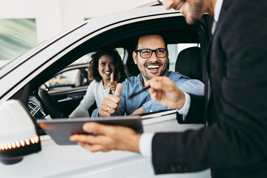 couple in car with salesman standing outside